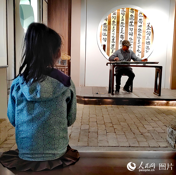 在西河古鎮(zhèn)弋農(nóng)古琴斫制工藝館內(nèi)，一位小朋友正在全神貫注地聆聽弋農(nóng)古琴非物質(zhì)文化遺產(chǎn)代表性傳承人翟光寶彈奏的古琴曲。翟光寶是弋農(nóng)古琴斫制工藝的第四代傳承人。弋農(nóng)古琴又稱“百納琴”，是以古木片合漆膠合而成的琴，始創(chuàng)于唐代。