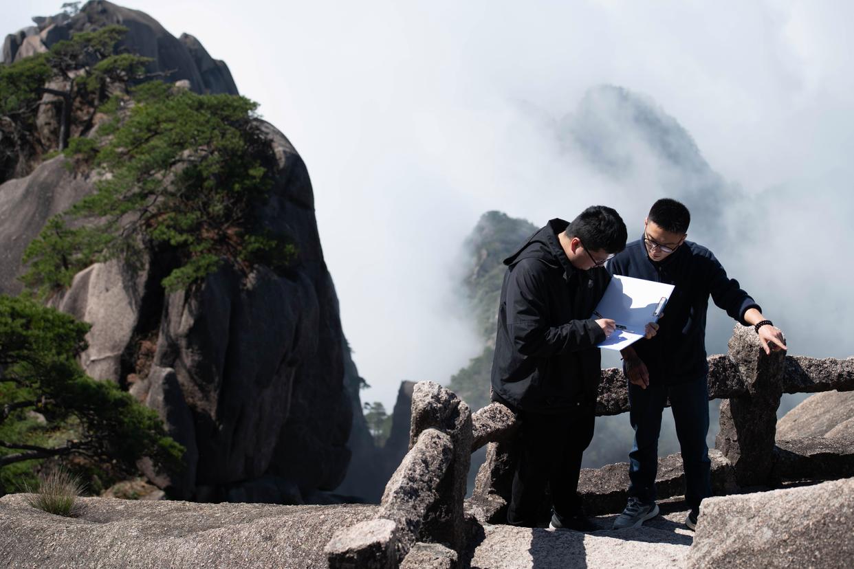 2025年4月23日，黃山風(fēng)景區(qū)文化事業(yè)管理辦公室副主任俞楊陽（右）與同事盛澤洋在封閉輪休中的蓮花峰記錄沿途石刻文物信息。新華社記者 張端 攝